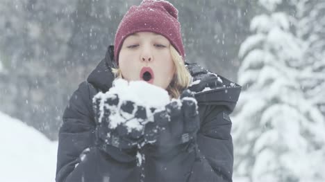 Close-up-shot-of-a-beautiful-young-Asian-woman-blowing-snow-towards-the-camera