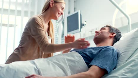 Im-Krankenhaus-besucht-glückliche-Ehefrau-Ehemann-erholt-sich,-liegend-auf-dem-Bett.-Sie-liebevoll-zu-umarmen-und-zu-Lächeln.