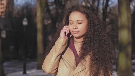 Mittlere-Aufnahme-einer-schönen-jungen-Frau-Gespräch-auf-ihr-Telefon-an-einem-Stadtpark