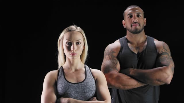 Portrait-shot-of-an-athletic-man-and-woman-crossing-their-arms-on-a-dark-background