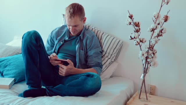 Young-man-looking-at-the-phone-screen,-relaxing-on-the-couch-in-the-room
