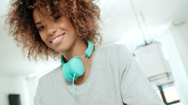 Glückliche-junge-Afro-Amerikanerin-mit-Kopfhörern-zu-einer-Kamera-posieren.
