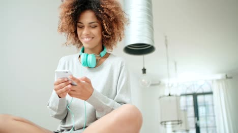 Schöne-junge-Afro-Amerikanerin-SMS-auf-dem-Handy-zu-Hause.