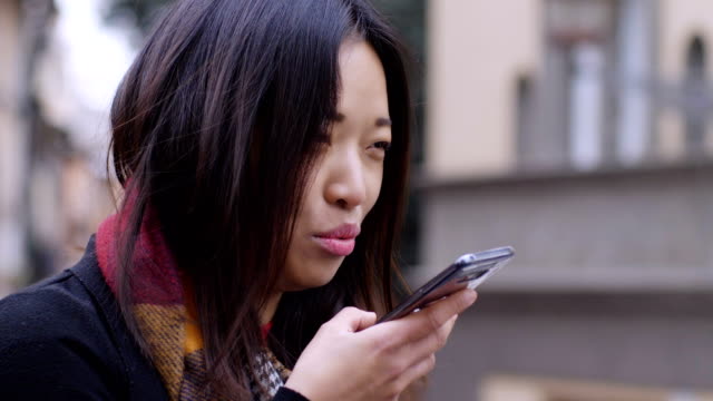Young-chinese-woman-talking-with-speaker-phone-in-the-street