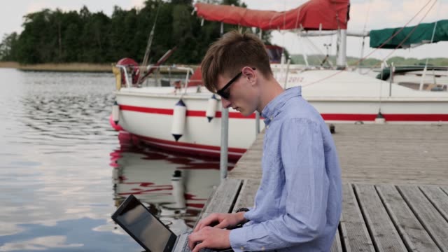 young-businessman-working-in-nontraditional-place-footbridge-.-confident-entrepreneur-remote-work-near-sailboat