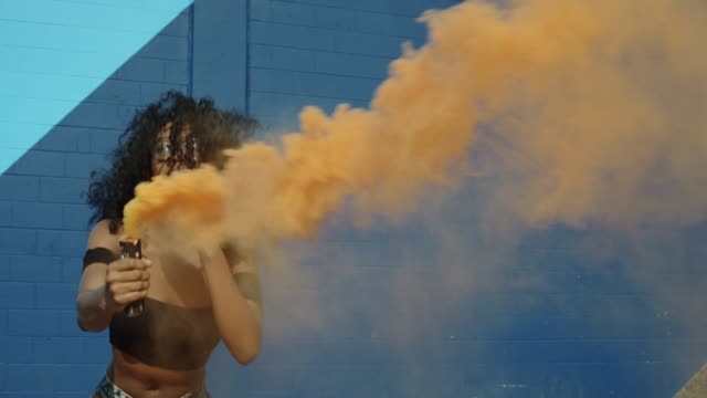 Schöne-junge-Frau-mit-bunten-Rauchgranate-tanzen-außerhalb-gegen-blaue-Wand