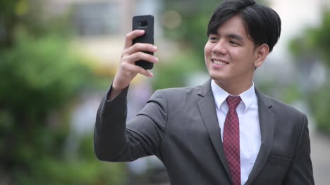 Young-handsome-Asian-businessman-using-phone-in-the-streets-outdoors
