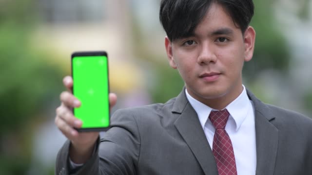 Young-handsome-Asian-businessman-showing-phone-in-the-streets-outdoors