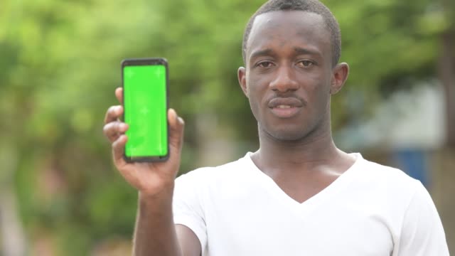 Young-happy-African-man-smiling-while-showing-phone-in-the-streets-outdoors