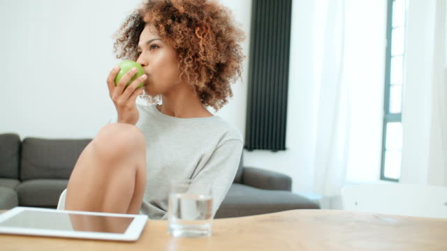 Young-woman-holding-green-apple-while-sitting-at-home.