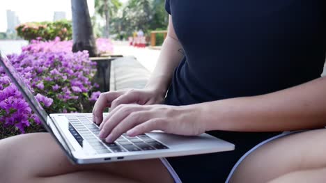 Schöne-asiatische-junge-Frau-sitzt-auf-der-Bank-im-Park-mit-Laptop.-Hübsche-Frau-auf-der-Suche-auf-ihrem-Computer-in-warmen-Frühlingstag.-Frauen-Lifestyle-Konzept.