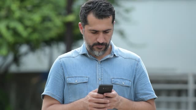 Gut-aussehend-persischen-bärtiger-Mann-mit-Handy-in-den-Straßen-im-freien
