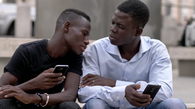 Juventud,-dispositivos-de-comunicación.--americano-africano-hombres-en-la-calle-usando-smartphon