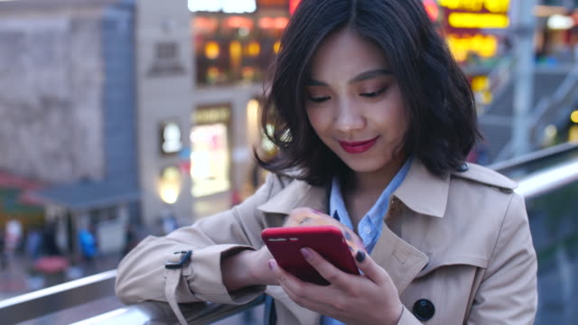Una-muy-feliz-asiático-joven-utilizando-el-teléfono-móvil-en-la-ciudad-en-la-noche