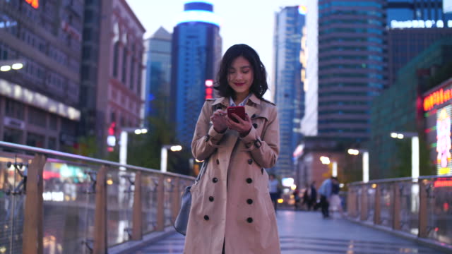 Slow-Motion-ziemlich-glücklich-junge-asiatische-Frau,-die-zu-Fuß-in-der-Stadtstraße-mit-Smartphone-am-Abend