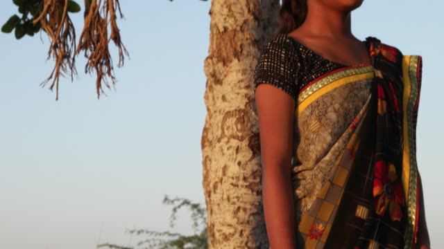 Schöne-indische-Teenager-Mädchen-warten-gerade-auf-einer-Anhöhe-unter-einem-Baum-an-einem-Sommertag-in-begierig-Liebe-Freude-freudig-Sonne-tropischen-heißen-hellen-Sonnenschein-Content-Blick-in-die-Kamera-handheld-stabilisiert