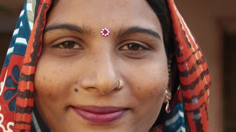 Extreme-close-up-of-a-gorgeous-Indian-woman's-face-smiling-laughing-happy-joy-jovial-looking-at-camera-in-traditional-dress-head-covered-bindi-pretty-jewelry-at-home-freedom-love-static-shot-lock-down