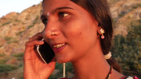 Handheld-shot-of-young-woman-talks-calls-mobile-phone-communication-device-connectivity-signal-wireless-smiles-happy-at-sunset-on-a-hill-outdoor-nature-hot-summer-day-magic-hour-beautiful-serene-love