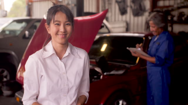 Portrait-of-smiling-customer-while-a-mechanic-works-on-a-car-in-the-background,-car-service-concept.-dolly-shot