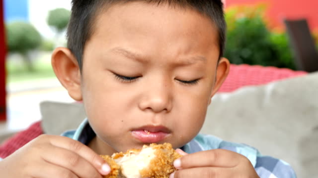 Niedlichen-asiatischen-jungen-freuen-uns-gebratene-Hähnchenschenkel-im-Restaurant-zu-essen.-4k-Video-Zeitlupe