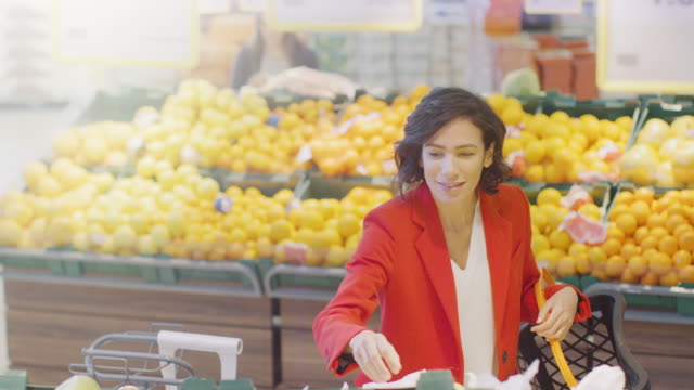 En-el-supermercado:-retrato-de-la-hermosa-sonriente-mujer-elegir-orgánica-de-frutas-en-el-pasillo-de-productos-frescos-y-pone-les-en-la-cesta-de-la-compra.-Alto-ángulo-tiro.