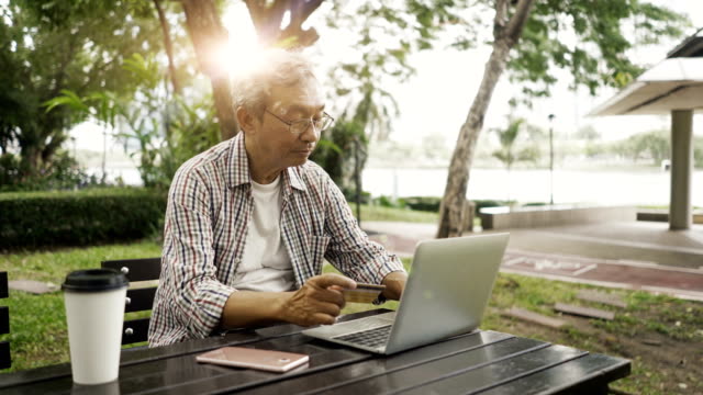 Asiatische-senior-woman-Online-shopping-mit-seinem-Notebook-im-park