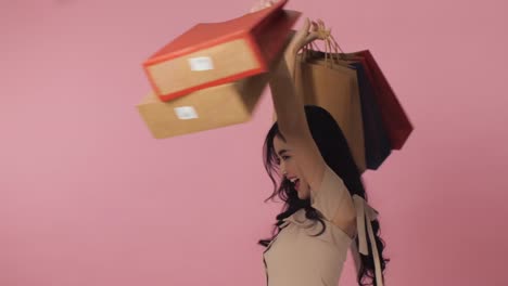 Retrato-de-sonriente-mujer-asiática-sobre-fondo-rosa-en-estudio.-Feliz-mujer-sosteniendo-un-montón-de-coloridos-bolsos-de-compras.-Concepto-de-venta-estacional.
