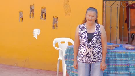 An-old-hispanic-woman-standing-in-front-of-an-orange-wall-in-Mexico