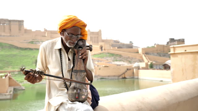 An-elderly-street-male-musician-playing-an-Indian-classical-music-instrument-beside-lake-in-Rajasthan