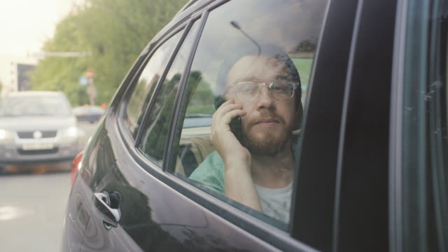 Handsome-Young-Man-Riding-on-a-Passenger-Seat-of-a-Car-Makes-a-Phone-Call,-Talks-with-Clients,-Customers-and-Business-Associates.-Camera-Shot-from-Outside-the-Vehicle.