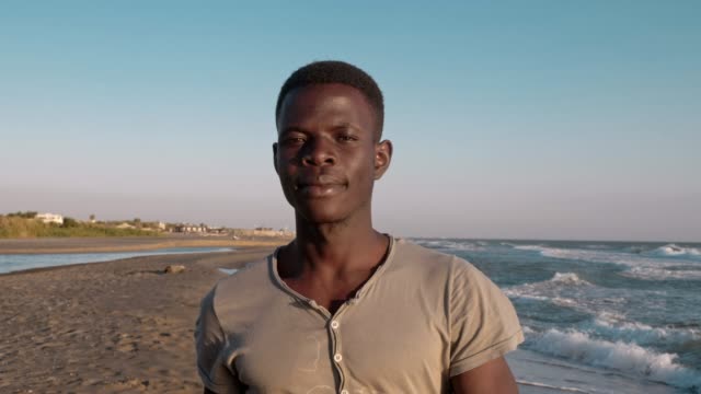 seria-seguro-negro-africano-hombre-solitario-caminando-por-la-playa-mirando-la-cámara