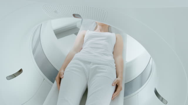 Mujer-paciente-acostado-en-una-tomografía-computarizada-o-resonancia-magnética,-cama-se-mueve-dentro-de-la-exploración-de-su-cuerpo-y-el-cerebro.-En-laboratorio-médico-con-equipos-de-alta-tecnología.-Tiro-de-cámara-elevada.
