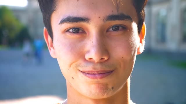 Cute-asian-man-close-up-smiling-in-braces-and-looking-at-camera-relaxed,-chill-mood,-outside,-sunshines