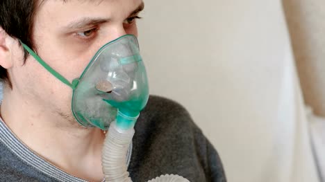 Use-nebulizer-and-inhaler-for-the-treatment.-Closeup-man's-face-inhaling-through-inhaler-mask.-Front-view.