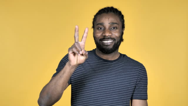 Victory-Sign-by-Casual-African-Man-Isolated-on-Yellow-Background