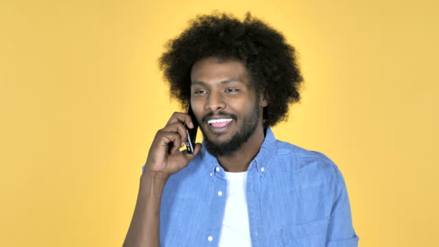 Hombre-afroamericano-hablando-en-teléfono-inteligente-sobre-fondo-amarillo