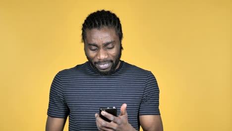 Legerer-afrikanischen-Mann-unter-Schock-bei-der-Verwendung-von-isolierten-Smartphone-auf-gelbem-Hintergrund