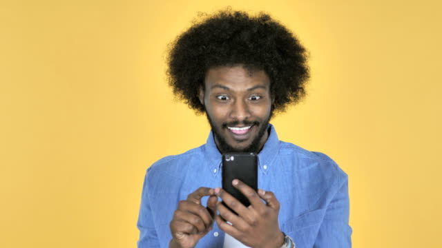 Hombre-afroamericano-emocionados-a-éxito-al-Smartphone-utilizando-sobre-fondo-amarillo