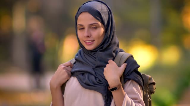 Close-up-portrait-of-Muslim-girl-in-hijab-watching-into-camera-with-smile,-showing-the-backpack.