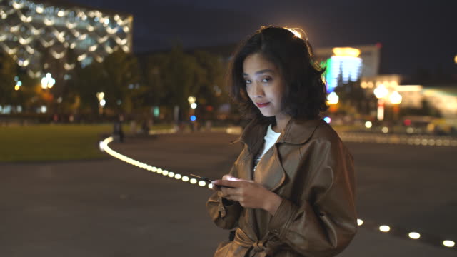 hübsche-junge-Asiatin-mit-Handy-in-der-Stadtstraße-in-der-Nacht,-4k