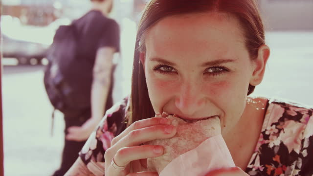 A-beautiful-girl-at-an-outdoor-table-eating-a-burrito-and-laughing,-slow-motion