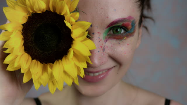 4k-la-foto-de-una-mujer-con-maquillaje-multicolor-con-girasol-(foco-en-flor)