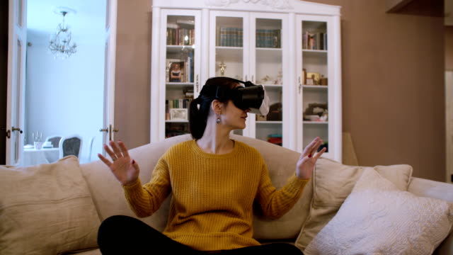 Beautiful-young-woman-sitting-on-sofa-at-living-room-and-using-VR-headset.-4K