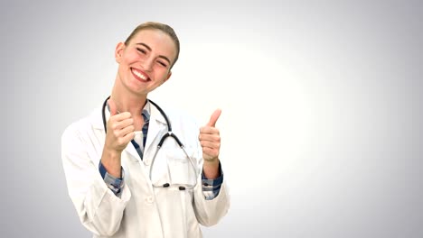Portrait-of-young-medical-doctor-woman-smiling,-giving-thumbs-up-hand-sign,-looking-at-camera-with-stethoscope-and-lab-coat-on-white-background