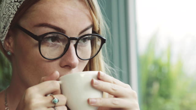 Beautiful-young-woman-drinking-coffee-in-cafe.-Girl-dreaming.-Female-wearing-glasses.