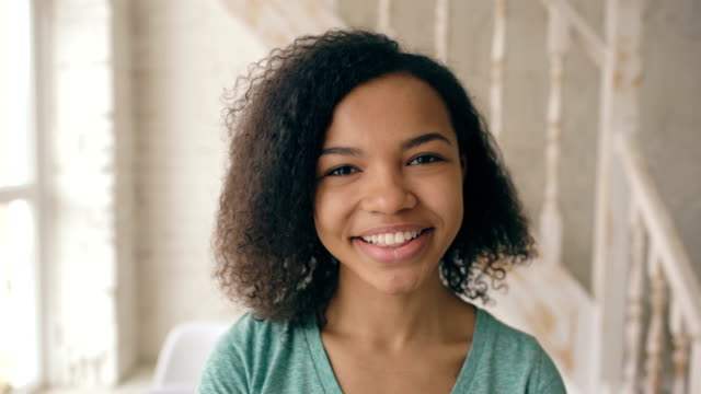 Closeup-portrait-of-beautiful-african-american-girl-laughing-and-looking-into-camera.-Teenager-show-emotions-from-serios-face-to-laugh-at-home