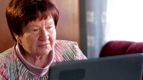 Una-mujer-mayor-comprueba-los-mensajes-en-las-redes-sociales-en-un-ordenador-portátil-en-casa.-Ella-se-sienta-en-la-mesa