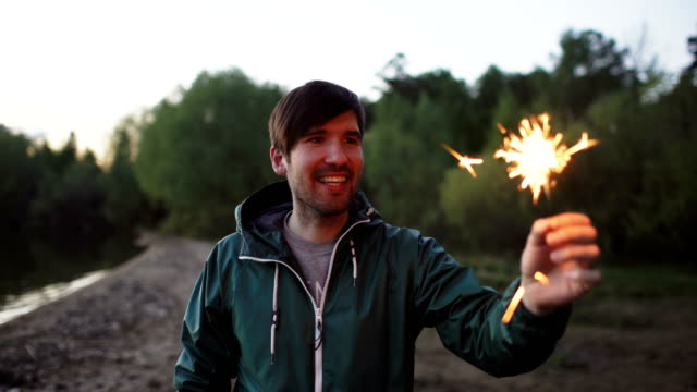 Portrait-of-young-smiling-man-with-sparkler-celebrating-at-beach-party