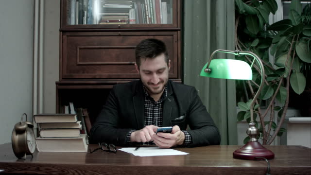 Junge-Schriftsteller-an-seinem-Schreibtisch-glücklich-messaging-auf-dem-Handy