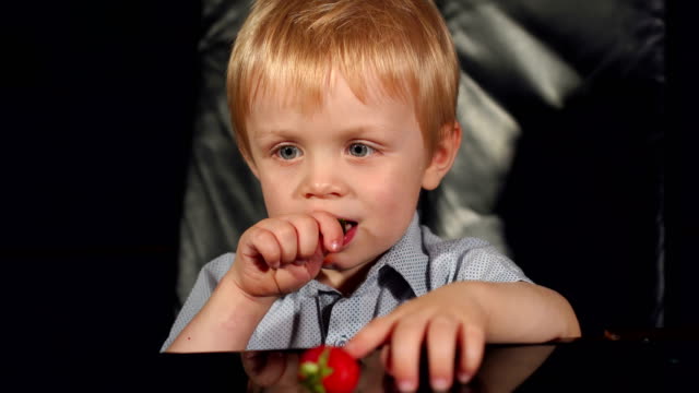 Little-boy-eating-strawberries-on-black-background